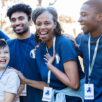 A group of volunteers with youth who are outside and smiling.